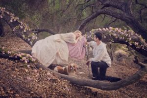 Prince and princess in the forest with a dog, man is kneeling while woman is lying down on a tree